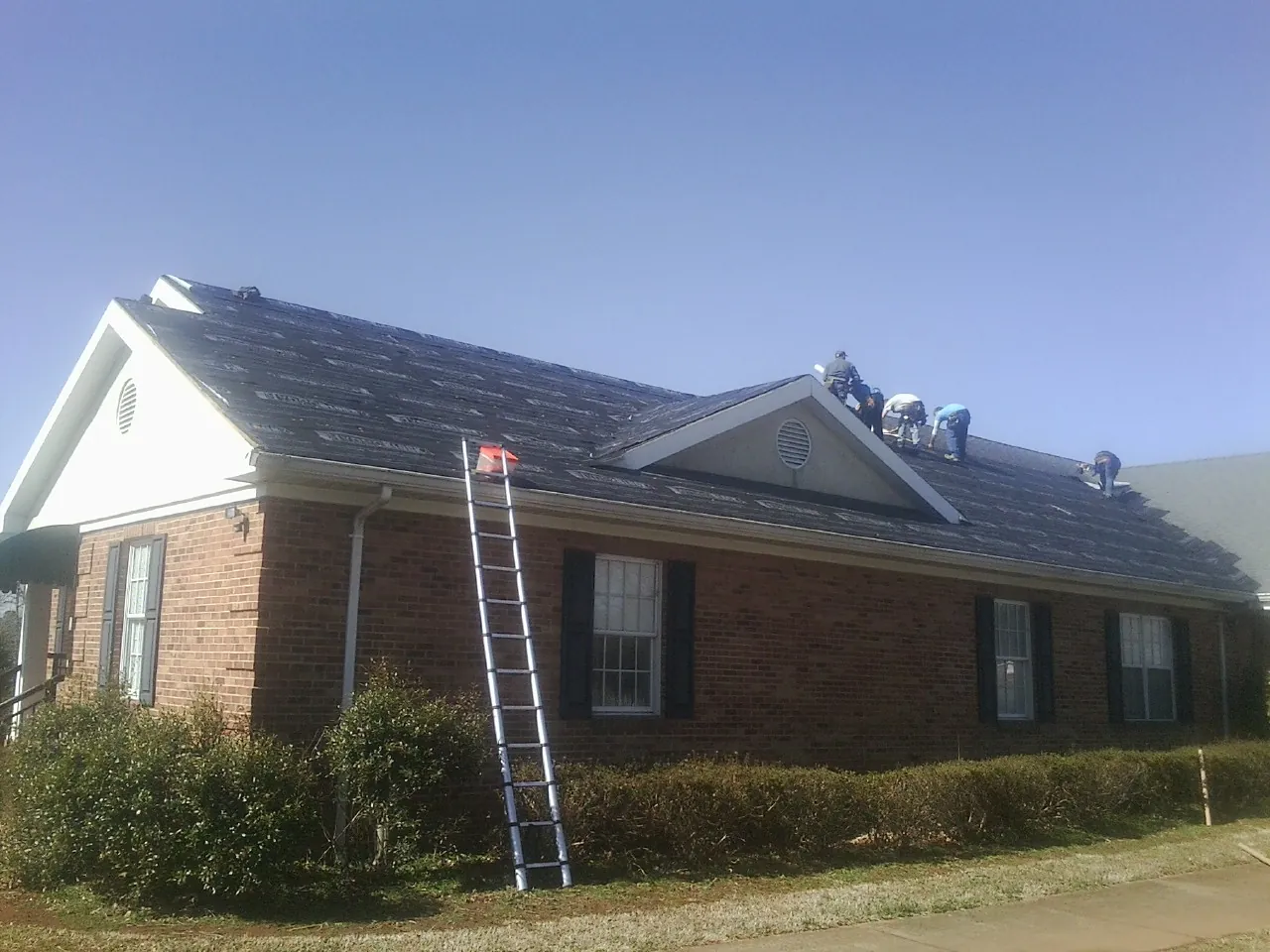 Crew tearing shingles off a brick ranch roof with a ladder set — Emergency Roof Repair work by our crew in Hampden