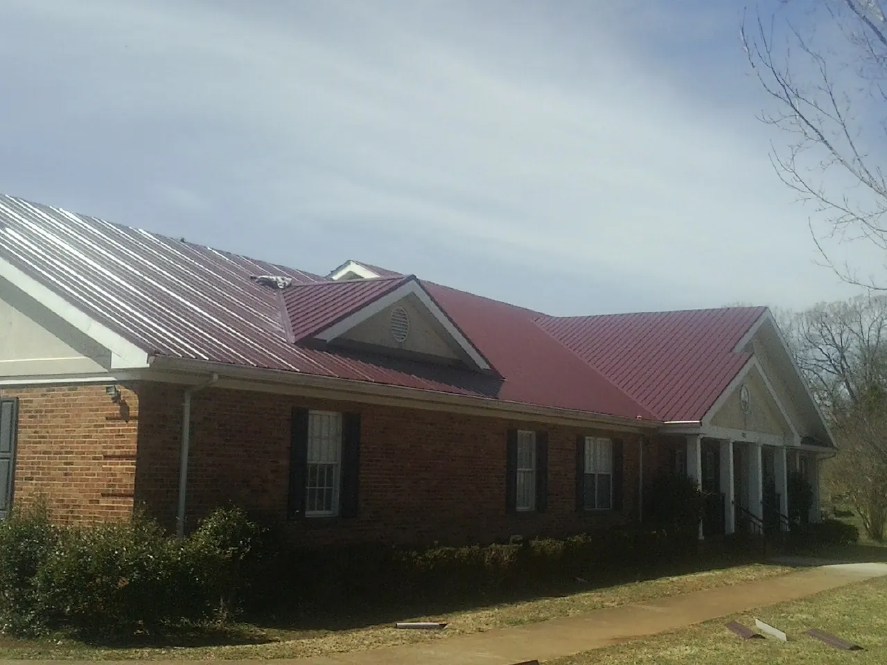 Red metal roof with gabled entries on a long brick building, from a Hail Damage Roof Repair job in Hampden