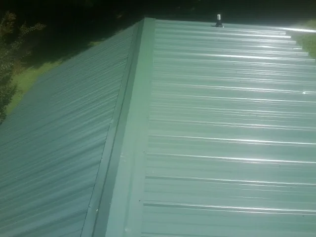 New green metal panels meeting at the ridge of a roof — Flat Roof Repair work by our crew in Hampden