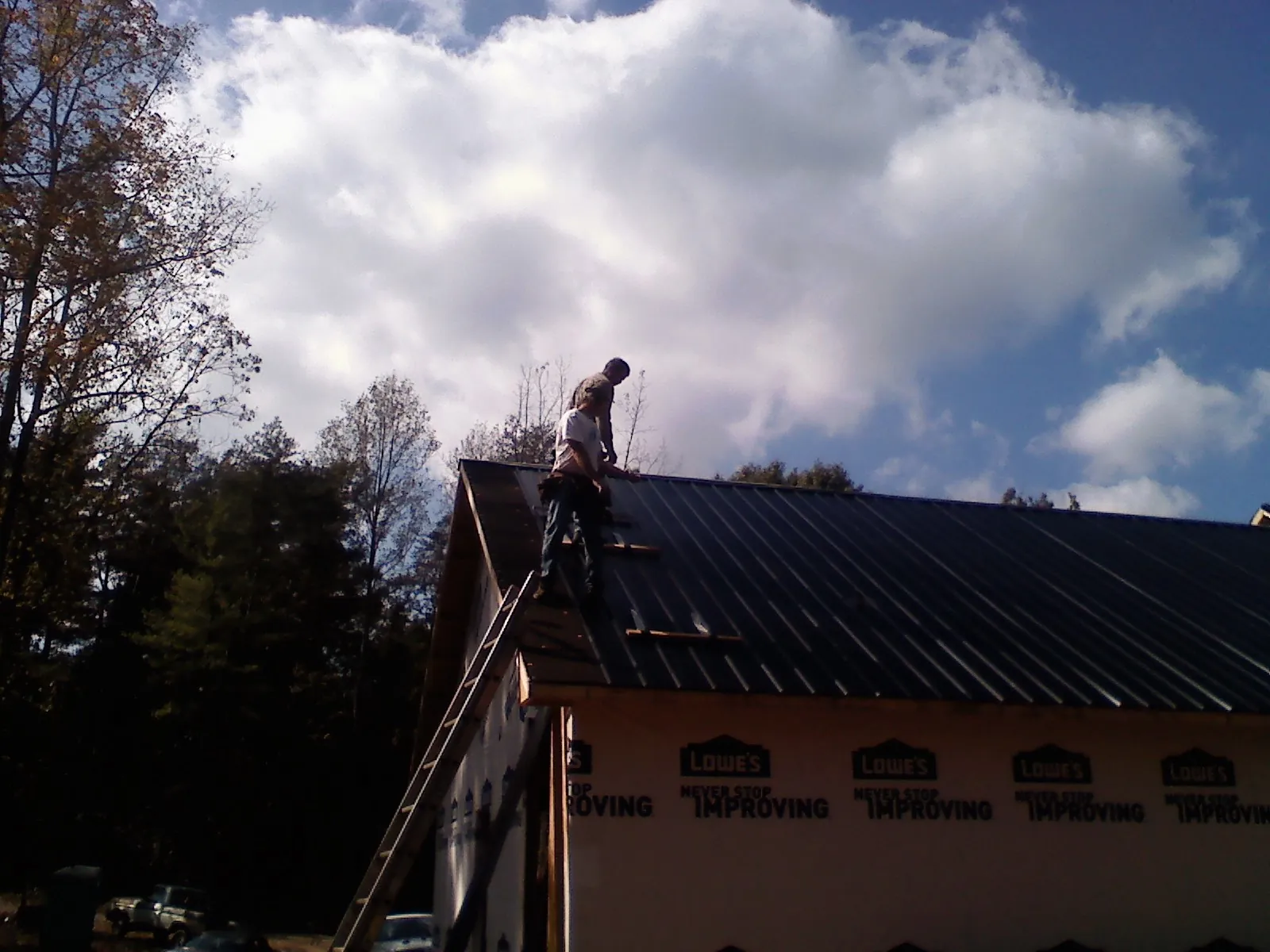 Roofer fastening dark metal panels high against a cloudy sky, from a Roof Inspection job in Hampden
