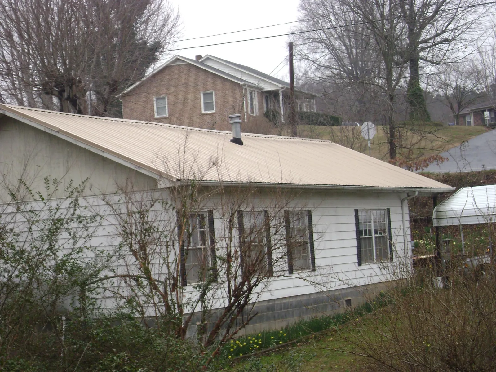 Tan metal roof on a white sided house set into a hillside — Commercial Roofing by Roofing Brothers in Hampden
