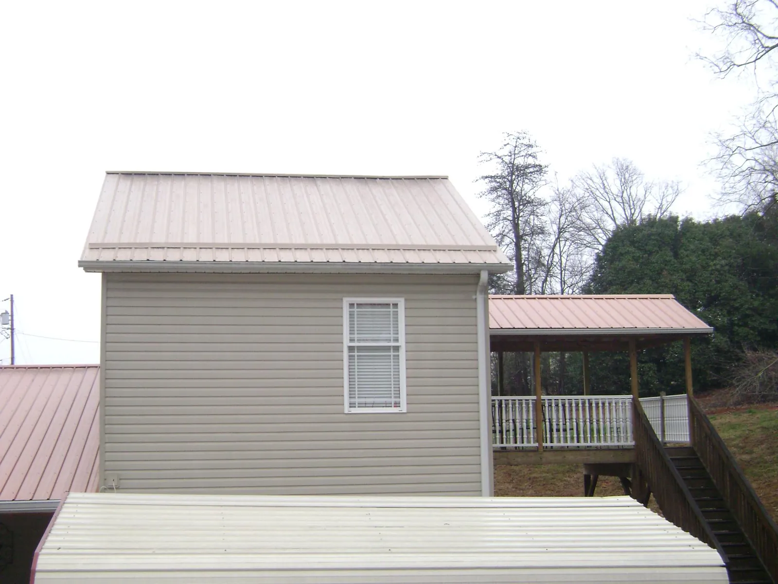 Tan metal roofs on a two story addition and attached porch, from a Roof Replacement job in Hampden
